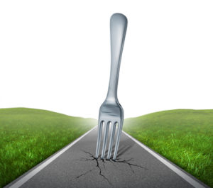 Fork in the road highway with a kitchen silverware metal fork metaphore with green grass and asphalt street representing the concept of journey and the challenges for future success.