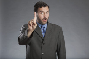 Businessman holding index finger up against gray background